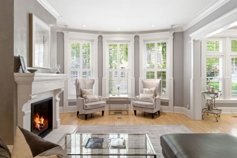 A stylish living room featuring plush armchairs, a fireplace, and bay windows with natural light streaming in.