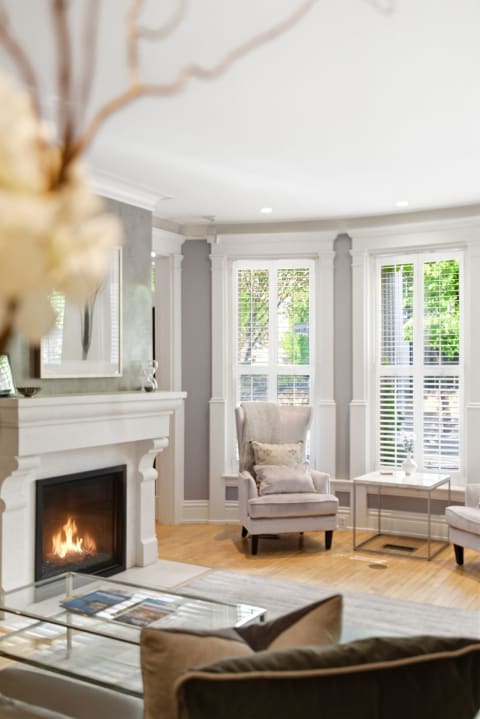 Elegant living room with a fireplace, plush chairs, and bay windows that let in natural light.