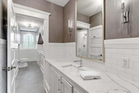 A modern bathroom featuring a marble countertop, white cabinetry, and gray tile flooring with elegant accents.