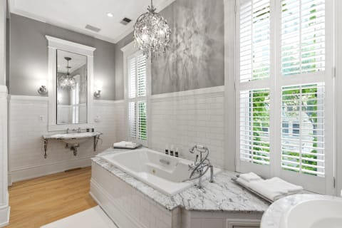 Luxurious bathroom with soaking tub, chandelier, and natural light from shutters.