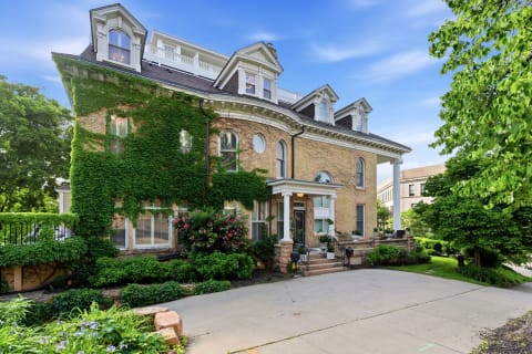 A historic brick home with ivy-covered walls, featuring elegant architectural details and surrounded by gardens.