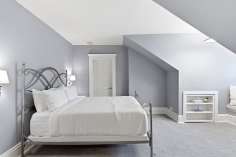 A tranquil attic bedroom featuring a metal bed frame, white linens, and soft gray walls with sloped ceilings.