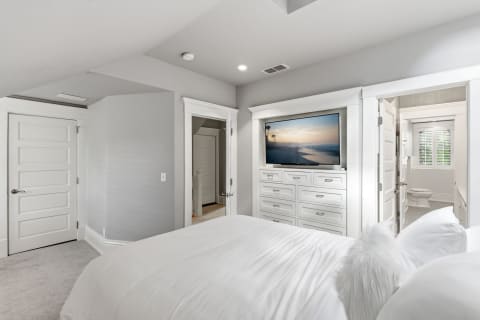 Tranquil bedroom featuring white linens and a built-in TV with a beach view.