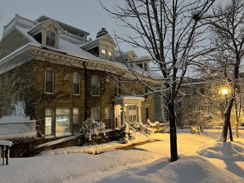 Historic house covered in snow with a glowing streetlamp and bare trees.