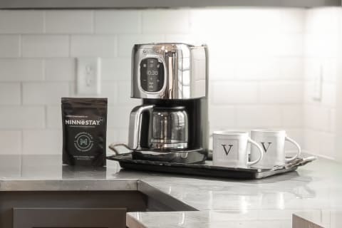 Modern kitchen counter with a coffee maker, coffee beans packet, and two white mugs on a slate tray.