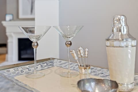 Two elegant martini glasses, a polished cocktail shaker, and decorative stirrers arranged on a silver tray.
