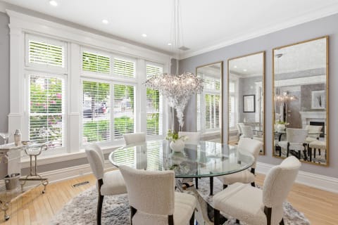 Elegant dining room featuring a round glass table, plush seating, and large windows with shutters.