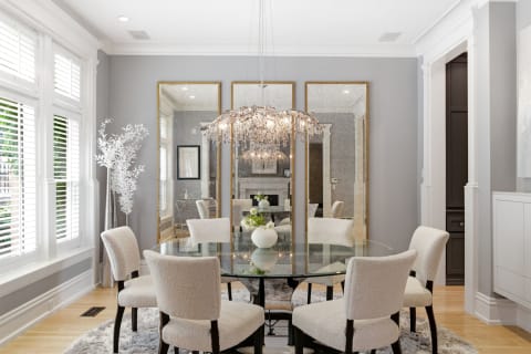 Elegant dining room with a glass table, plush chairs, and a crystal chandelier.