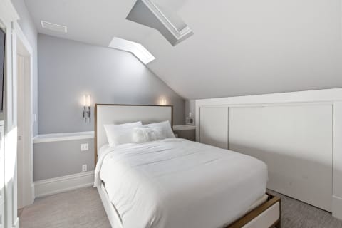 A modern bedroom with a bed, skylights, and minimalistic decor, creating a tranquil atmosphere.