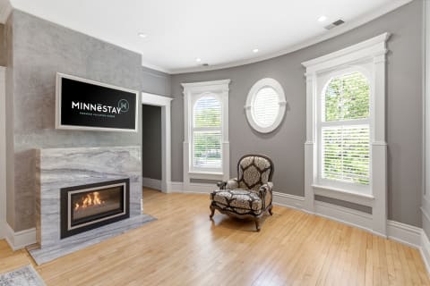 A stylish living area with a modern fireplace, an elegant armchair, and decorative gray walls, complemented by large windows.