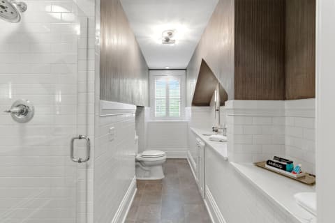 Modern bathroom with white subway tiles and marble countertops, showcasing a shower and neatly arranged toiletries.