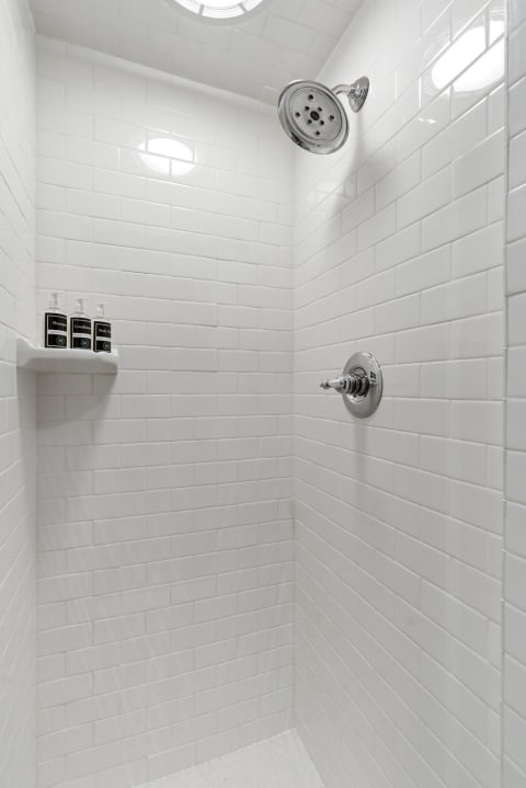 A minimalist walk-in shower with white subway tiles and a polished chrome showerhead.