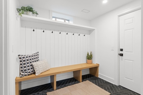 Modern entryway with a bench, pillows, hooks, and plants.