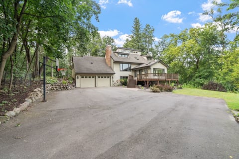 A serene two-story house with a driveway and basketball hoop set in a lush green environment.