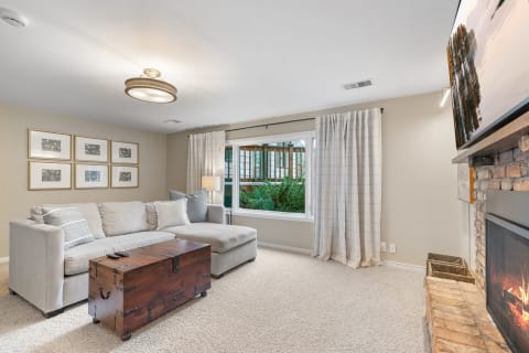 A comfortable living room with a sectional sofa, wooden trunk, fireplace, and green view outside.
