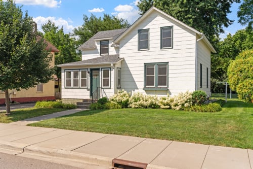 Charming white home surrounded by mature trees and landscaped gardens in a peaceful residential neighborhood.