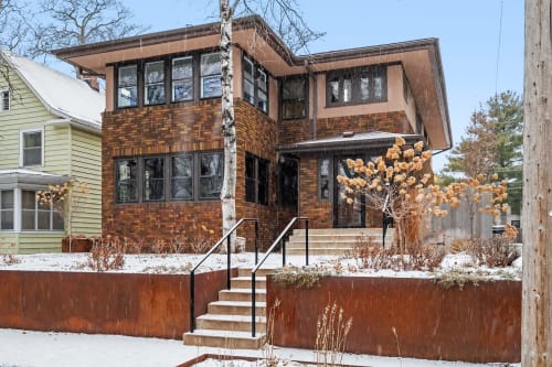 A charming brick duplex sits in a quiet residential neighborhood, showcasing beautiful architectural details against a winter backdrop.
