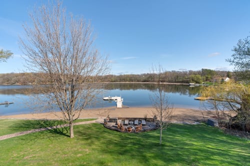 Pristine lakefront property with private dock, fire pit area, and expansive lawn leading to crystal-clear waters.