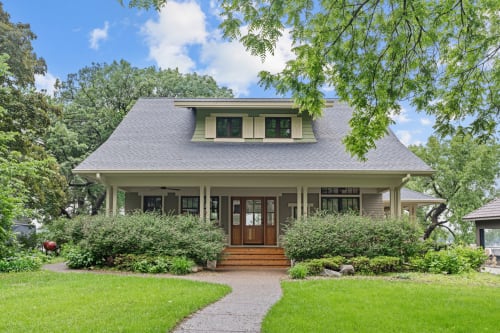 Charming Craftsman home nestled among mature trees with welcoming front porch and manicured landscaping in a peaceful residential setting.